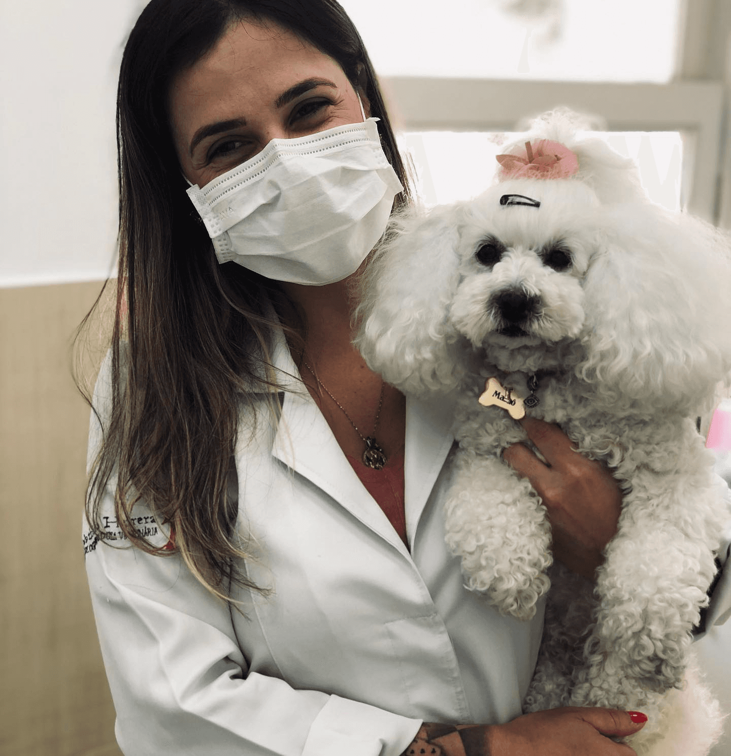 Nathália Herrera de jaleco segurando um cão bichon durante a consulta